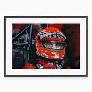 Könnte beinhalten: Gerahmter Druck eines Formel-1-Fahrers mit rotem Rennhelm. Der Helm trägt die Logos Marlboro und BOSS. Der Fahrer trägt einen roten Rennanzug und sitzt in einem Rennwagen.