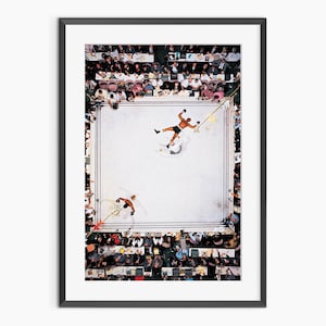 Puede incluir: Impresión enmarcada de un combate de boxeo desde arriba. Dos boxeadores están en el ring, uno está en el suelo. El ring está rodeado de espectadores. La imagen es en color y tiene un aspecto vintage.