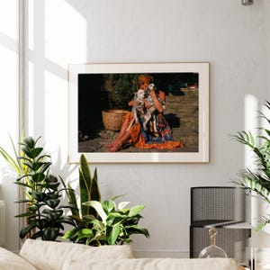 A framed photograph of a woman sitting on a stone step, holding a small dog, is hanging on a white wall in a living room.