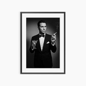 May include: Monochrome framed print of a man in a tuxedo, holding a martini and a lit cigarette. The man wears a bow tie and a white pocket square. The image has a vintage, classic feel, reminiscent of a bygone era.