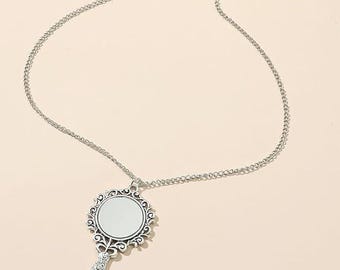 May include: Silver-coloured necklace with a pendant shaped like a hand mirror. The mirror has an ornate, decorative frame and a small, round reflective surface. The chain is delicate and the pendant hangs from the center. The necklace is displayed on a neutral background.