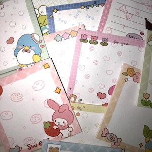 Op de afbeelding: Een verzameling kleurrijke, bedrukte memoblokken. Ontwerpen omvatten stripfiguren, harten, sterren en bloemmotieven. Sommige blokken hebben roze randen en de tekst "for you."