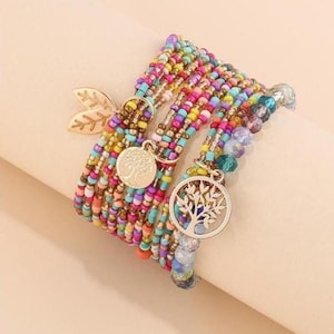 May include: A collection of beaded bracelets in a range of colours, including pink, yellow, blue, and green. Each bracelet features small, colourful beads and decorative charms, such as a gold leaf and tree of life pendants. The bracelets are designed for wrist wear.