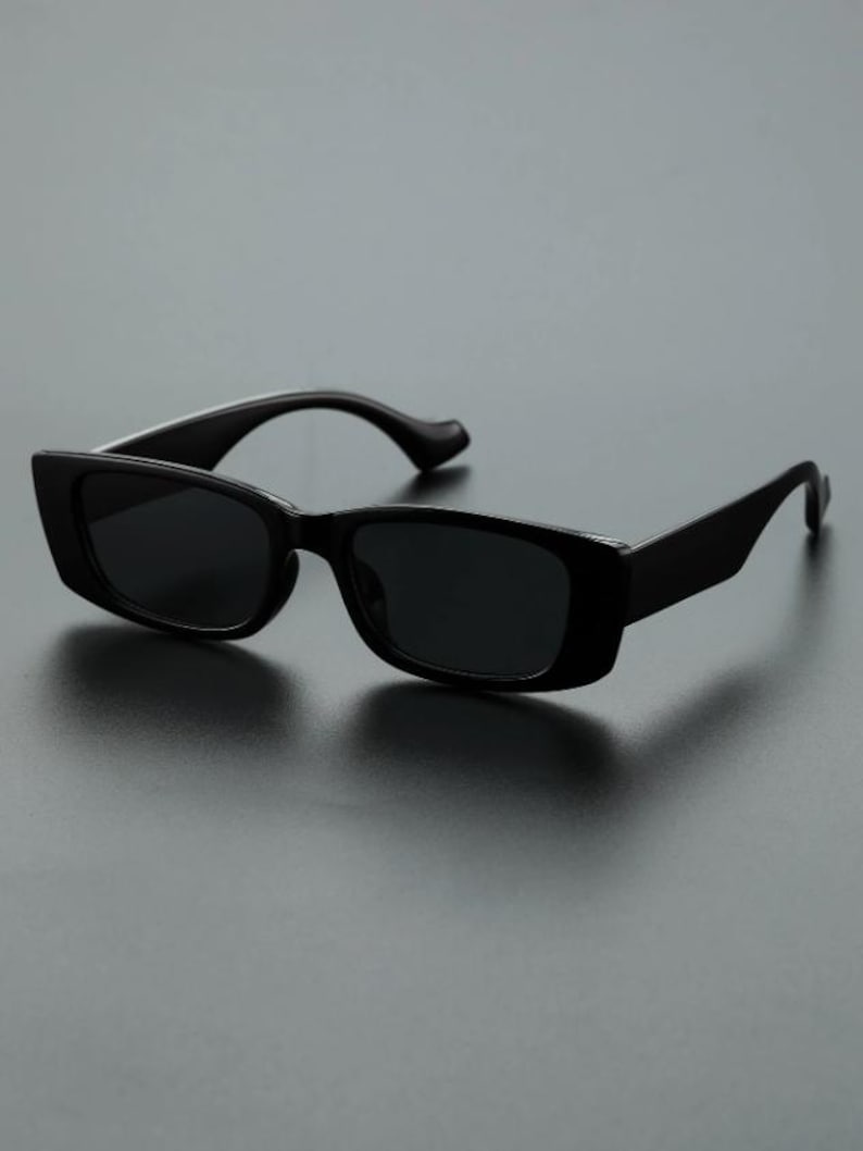 May include: Black rectangular sunglasses with dark lenses. The sunglasses have a thick, solid frame and curved temples. The design is simple and modern, suitable for various styles.