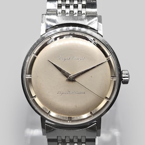 Può includere: Un orologio da polso Royal Orient vintage con cinturino e cassa in metallo argentato. Il quadrante dell'orologio è color crema chiaro con lancette nere e la scritta "Royal Orient" e "23 Jewels Antishock".