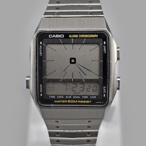 Può includere: Un orologio digitale Casio argentato con quadrante rettangolare e cinturino in metallo. L'orologio mostra l'ora 7:23:20. Sul quadrante è presente la scritta "CASIO ALARM CHRONOGRAPH" e "WATER 50M RESIST".