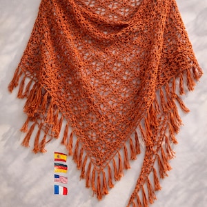 Op de afbeelding: Een roestkleurige, gehaakte sjaal met een driehoekige vorm en franjes. Het open weefsel is zichtbaar over de hele sjaal. De franjes hangen aan de onderkant. De sjaal wordt gepresenteerd op een wit oppervlak.