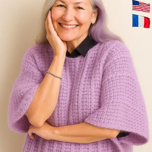 May include: A woman wearing a lilac-colored, textured knit sweater with a black collared shirt underneath. She is also wearing a silver bracelet. The image includes flags of Spain, Germany, the United States, and France.