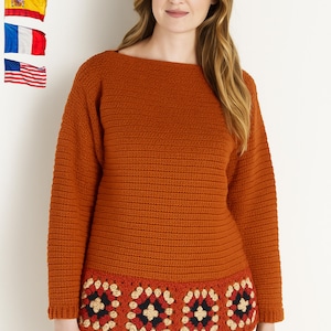 Puede incluir: Un suéter de manga larga color óxido con cuello barco. El dobladillo inferior presenta un patrón decorativo de ganchillo en rojo, negro y crema. El suéter está hecho de una tela de punto texturizada, ideal para otoño o invierno.