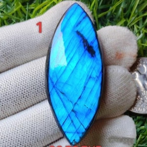 Pode incluir: Uma gema azul vibrante com uma forma alongada única. A pedra exibe um jogo de luz marcante, com padrões internos visíveis. O texto "1" é visível. O texto "GO TO THE NEXT PAGE TO SEE MORE OPTIONS" também é visível.