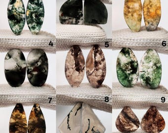 May include: A collection of nine pairs of polished gemstone cabochons. The stones display a variety of colors, including green, brown, white, and yellow, with unique patterns and textures. The shapes vary from oval to teardrop.