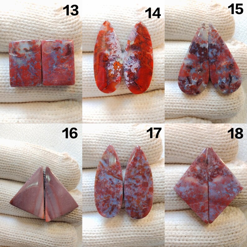 May include: A collection of six pairs of polished gemstone cabochons in various shapes. The stones display a mix of red, white, and blue hues, with unique patterns and textures. Each pair is displayed on a white fabric background.