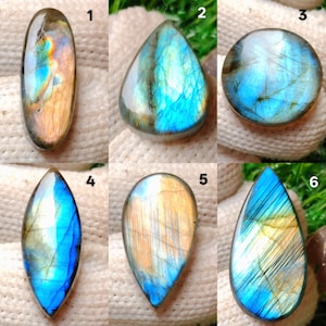 May include: A collection of six polished labradorite gemstones in various shapes. The stones display iridescent flashes of blue, gold, and orange. Each stone is unique, with variations in color and pattern. The gemstones are displayed on a white surface.