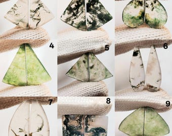 May include: A collection of nine pairs of polished gemstone cabochons. The stones feature various shapes, including triangles, teardrops, and rounded forms. The colors range from clear to white, with green and black inclusions, creating unique patterns.