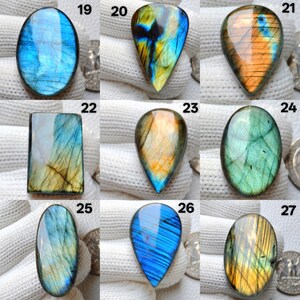 May include: A collection of polished labradorite gemstones in various shapes, including oval, teardrop, and rectangular. The stones display iridescent flashes of blue, green, yellow, and orange. Each stone is unique, showcasing natural patterns and colors.