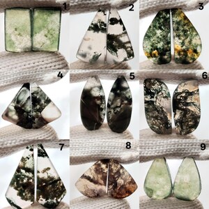 May include: A collection of nine pairs of polished gemstone cabochons. The stones display a variety of shapes, including rectangles, triangles, and teardrops. The colors range from clear to green, brown, and white, with intricate internal patterns.