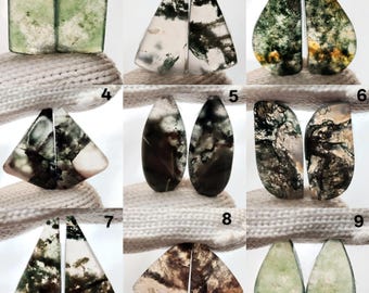 May include: A collection of nine pairs of polished gemstone cabochons. The stones display a variety of shapes, including rectangles, triangles, and teardrops. The colors range from clear to green, brown, and white, with intricate internal patterns.