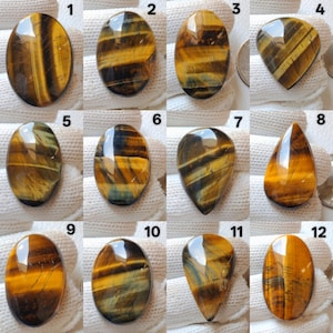 May include: Twelve polished tiger's eye gemstones in various shapes, including oval, teardrop, and triangular. The stones display a mix of golden brown, yellow, and black bands. Each stone is unique, with variations in colour and pattern.