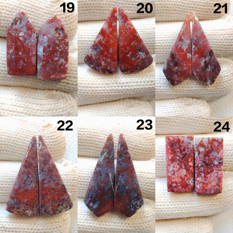 May include: A collection of six pairs of polished gemstones, each with a unique shape and pattern. The stones display a mix of red, white, and blue hues, with visible veining and marbling. The gemstones are arranged on a white, textured surface.