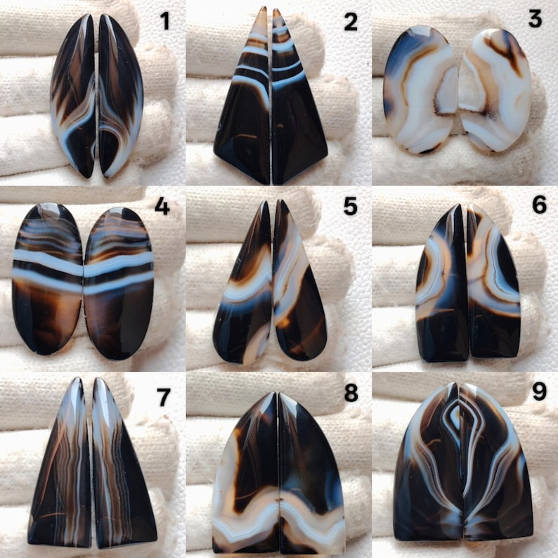 May include: Nine pairs of polished agate gemstones in various shapes, including oval, triangular, and teardrop. The stones feature a mix of black, brown, white, and blue banding patterns. Each pair is split down the middle, showcasing the symmetrical designs.