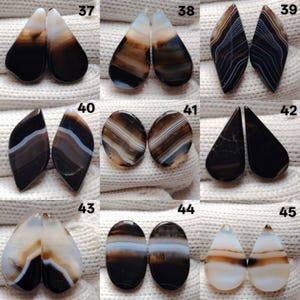 May include: Nine pairs of polished agate gemstones are displayed, showcasing a variety of shapes such as teardrops and ovals. The stones feature bands of brown, black, white, and blue. Each pair is numbered for easy reference.