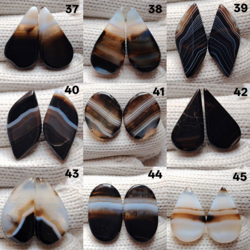 May include: Nine pairs of polished agate gemstones are displayed, showcasing a variety of shapes such as teardrops and ovals. The stones feature bands of brown, black, white, and blue. Each pair is numbered for easy reference.