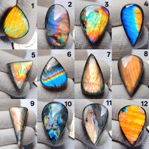 Op de afbeelding: Een verzameling van twaalf gepolijste labradoriet edelstenen in verschillende vormen. De stenen vertonen iriserende kleuren, waaronder blauw, oranje, geel en groen. Elke steen is uniek, met variaties in kleur en patroon, geschikt voor het maken van sieraden of verzamelen.