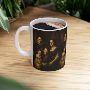 Op de afbeelding: Witte keramische mok met een klassiek familieportret. Het kunstwerk toont een groep mensen in historische kleding. De mok bevat een donkere vloeistof, waarschijnlijk koffie of thee, en staat op een houten oppervlak.