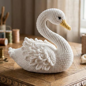 May include: A handcrafted white crochet swan with a yellow beak and black eyes. The swan is sitting on a wooden surface. The swan's wings have a textured, layered design. The swan is a decorative item.