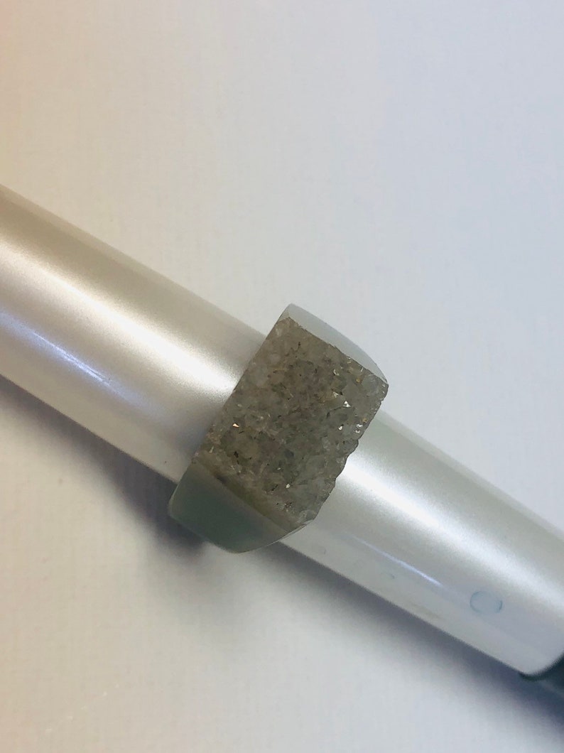 K&ouml;nnte beinhalten: Ein silberner Ring mit einem klaren, facettierten Stein, der in der Mitte eingesetzt ist. Der Stein ist rechteckig und hat eine raue, strukturierte Oberfl&auml;che.