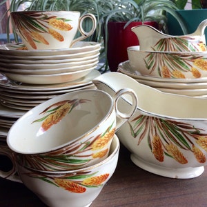 May include: A set of vintage cream-colored china with a gold trim and a floral pattern featuring brown, yellow, and green leaves and flowers. The set includes a teapot, creamer, sugar bowl, and cups and saucers.