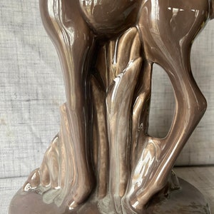 May include: A brown ceramic deer figurine standing on a base with a leafy design. The deer is glazed with a glossy finish.