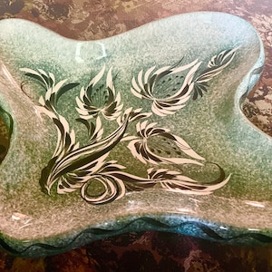 May include: A green ceramic serving dish with a wavy edge and a black and white floral design.