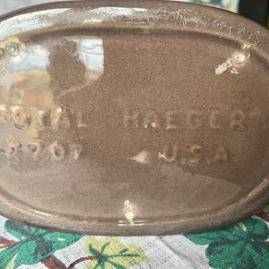 May include: Close-up of the bottom of a brown ceramic pitcher with the text "Royal Haeger 5707 USA" stamped on the bottom.