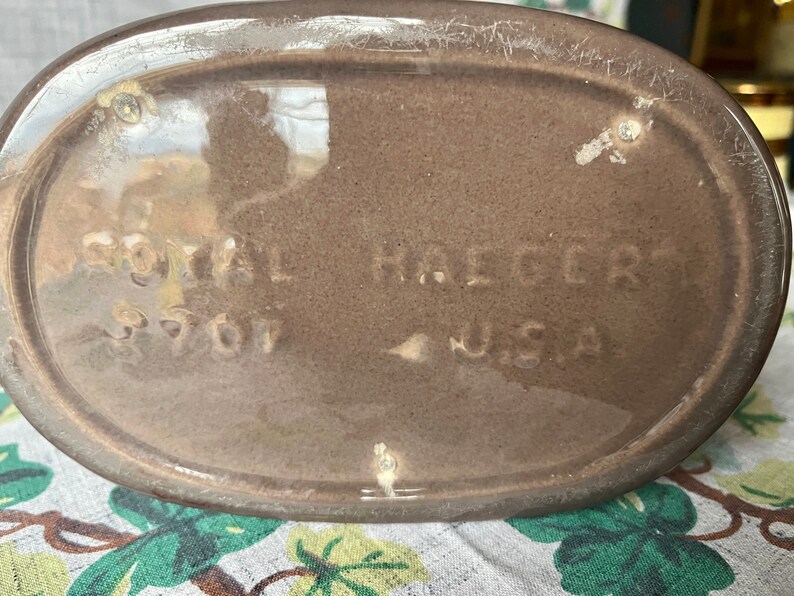 May include: Close-up of the bottom of a brown ceramic pitcher with the text "Royal Haeger 5707 USA" stamped on the bottom.