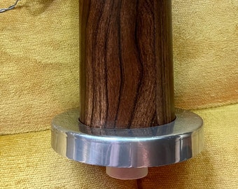 May include: A wooden dowel with a silver metal ring at the bottom. The dowel has a dark brown wood grain pattern.