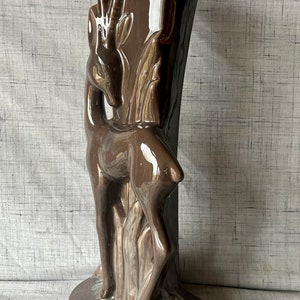 May include: A brown ceramic vase shaped like an antelope with a glossy finish. The vase is tall and slender with a wide base.