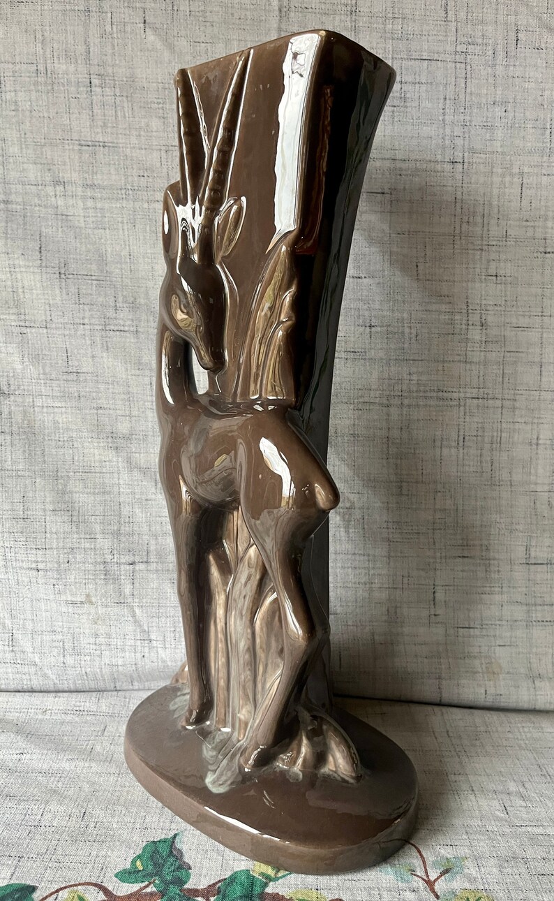 May include: A brown ceramic vase shaped like an antelope with a glossy finish. The vase is tall and slender with a wide base.