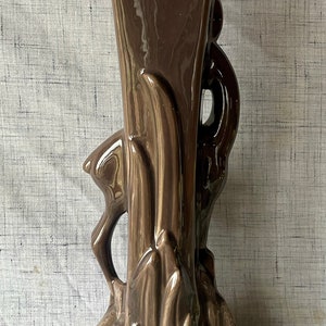 May include: A brown ceramic vase with a stylized bird design. The vase has a wide base and a narrow neck.