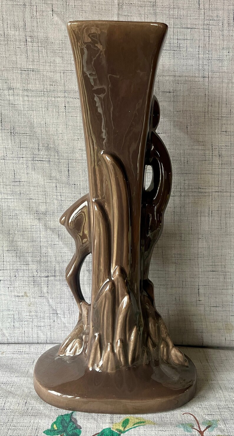 May include: A brown ceramic vase with a stylized bird design. The vase has a wide base and a narrow neck.