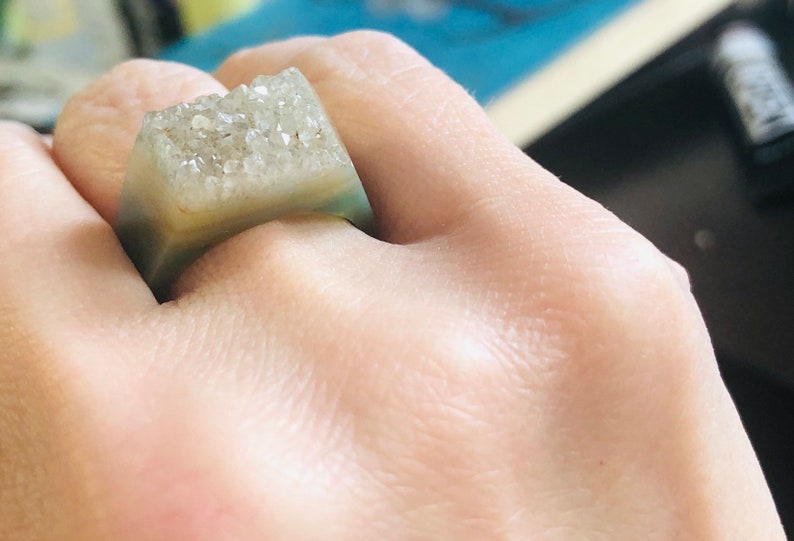 K&ouml;nnte beinhalten: Ein quadratischer Ring mit einer klaren, hellgr&uuml;nen Harzbasis und einer oberen Schicht aus wei&szlig;en, glitzernden Kristallen.