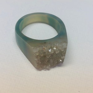 K&ouml;nnte beinhalten: Ein hellblauer Ring aus Harz mit einem Cluster aus wei&szlig;en Kristallen auf der Vorderseite.