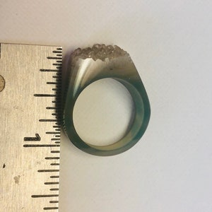 K&ouml;nnte beinhalten: Ein gr&uuml;ner Achatring mit einem klaren Quarzkristall-Cluster auf der Oberseite. Der Ring hat einen Durchmesser von etwa 2,5 cm.