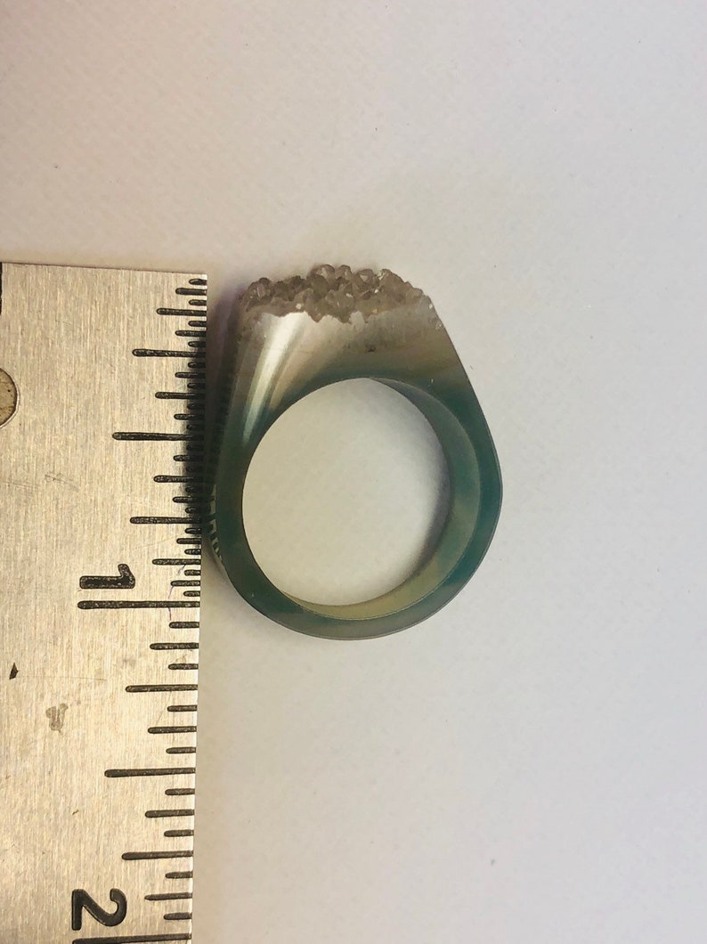 K&ouml;nnte beinhalten: Ein gr&uuml;ner Achatring mit einem klaren Quarzkristall-Cluster auf der Oberseite. Der Ring hat einen Durchmesser von etwa 2,5 cm.