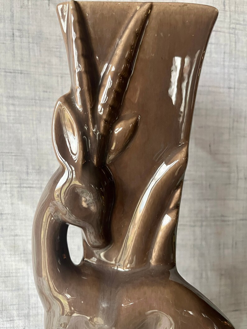 May include: A brown ceramic vase shaped like an antelope with a glossy finish.