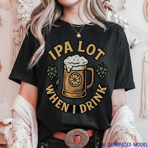 May include: A black short-sleeve t-shirt featuring a graphic of a beer mug with foam and a citrus slice. The text reads IPA LOT WHEN I DRINK in a circular yellow font. Two green hop illustrations are positioned on either side of the beer mug.
