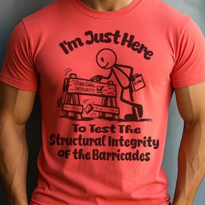 以下が含まれることがあります： 面白いグラフィックがプリントされた、コーラルカラーのTシャツ。デザインは、「Structural Integrity」と書かれたバリケードを検査している棒人間です。上部には「I'm Just Here」、下部には「To Test The Structural Integrity of the Barricades」と書かれています。