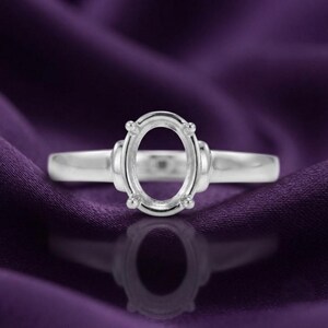 Könnte beinhalten: Eine Ringfassung aus silberfarbenem Metall mit einem ovalen Kopf, der zur Aufnahme eines Edelsteins konzipiert ist. Der Ring verfügt über eine glatte, polierte Ringschiene und vier Krappen, die vom ovalen Rahmen ausgehen, um einen Stein zu halten.