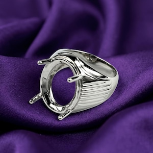 Könnte beinhalten: Eine polierte silberfarbene Ringfassung mit einer ovalen Mittelhalterung und vier Krappen zur Aufnahme eines Edelsteins. Die Ringschiene weist an der Seite des Metallschafts eine Reihe paralleler horizontaler Rillen auf.