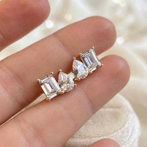 Può includere: Orecchini a lobo in oro con pietre preziose chiare di forma rettangolare e a goccia. Gli orecchini sono incastonati in oro. Le pietre preziose sono su uno sfondo chiaro.